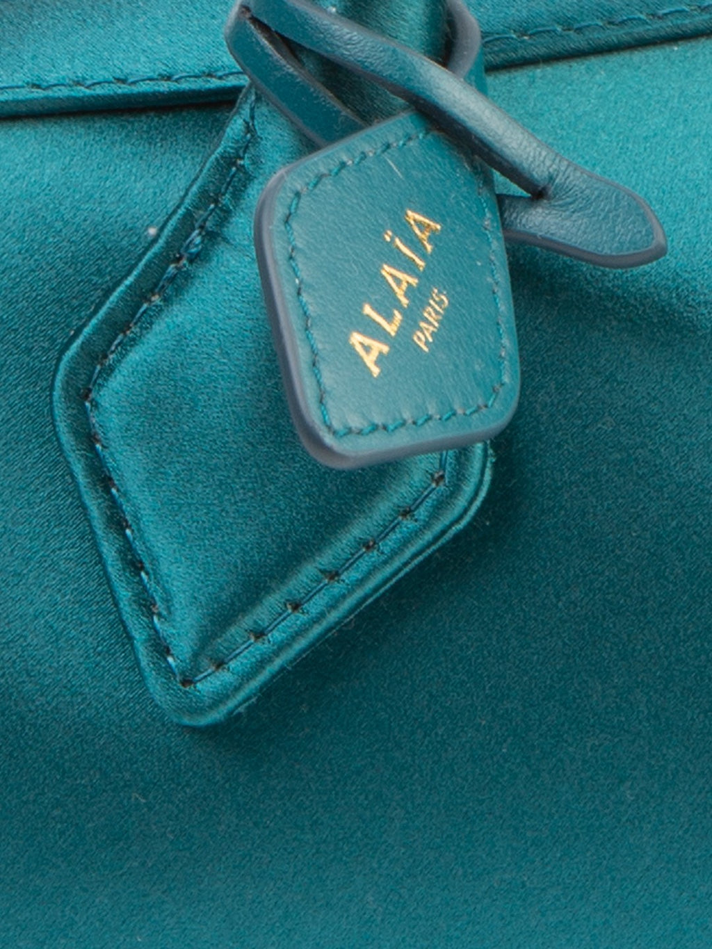 Bolsa Alaïa Le Teckel Small, cetim esmeralda, detalhe em macro da etiqueta original com a gravação ALAÏA PARIS, junto à base da alça — Domus Giulietta