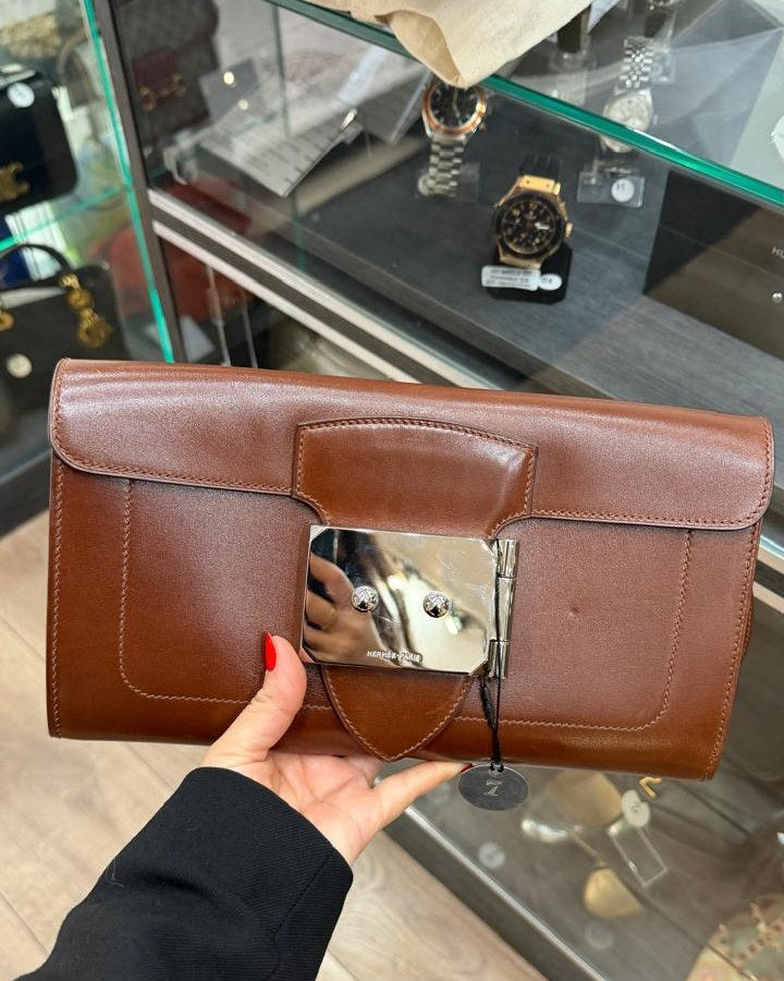 Bolsa de couro marrom com etiqueta pendurada, segurada na mão sobre o balcão de vidro de uma loja