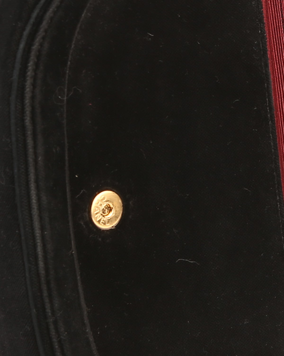 Veludo preto de costuras arqueadas, o botão de pressão dourado e, na borda, o forro em tecido bordô — Domus Giulietta